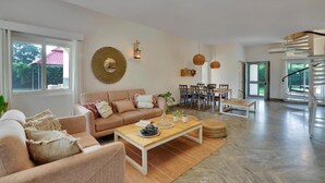 A spacious living area with a sofa, coffee table, and dining table. There is a staircase leading to an upper level. - Alaya Stays By Elivaas Luxe Farm Acre - Manesar (Taoru)
