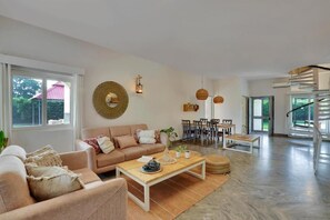 A spacious living area with a sofa, coffee table, and dining table. There is a staircase leading to an upper level. - Alaya Stays By Elivaas Luxe Farm Acre - Manesar (Taoru)