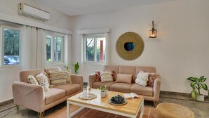 A living room with two sofas, a coffee table, and a wall-mounted light fixture. - Alaya Stays By Elivaas Luxe Farm Acre - Manesar (Taoru)