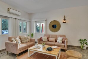 A living room with two sofas, a coffee table, and a wall-mounted light fixture. - Alaya Stays By Elivaas Luxe Farm Acre - Manesar (Taoru)