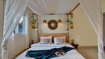 A bedroom with a canopy bed, a wooden headboard, two hanging lanterns, and a decorative sunburst mirror on the wall.