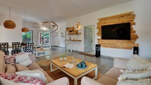 A modern living room with a wooden coffee table, beige sofas, and a TV mounted on a wooden wall. - Alaya Stays By Elivaas Luxe Farm Acre - Manesar (Taoru)