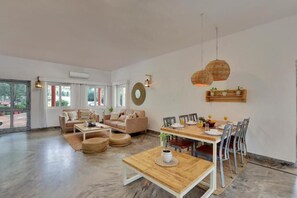 A spacious living area with a wooden dining table, two sofas, and a coffee table. - Alaya Stays By Elivaas Luxe Farm Acre - Manesar (Taoru)