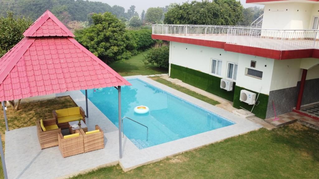 Une piscine avec un kiosque à toit rouge, un bâtiment blanc également doté d’un toit rouge, et une pelouse verte.