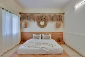 A bedroom with a wooden headboard, a large bed with white bedding, a woven wall hanging, and two wall-mounted lamps. - Alaya Stays By Elivaas Luxe Farm Acre - Manesar (Taoru)