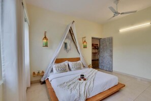 A bedroom with a canopy bed, two wall-mounted lanterns, a ceiling fan, and a door leading to another room. - Alaya Stays By Elivaas Luxe Farm Acre - Manesar (Taoru)