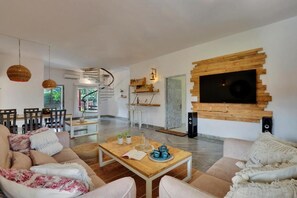 A modern living room with a wooden coffee table, beige sofas, and a TV mounted on a wooden wall. - Alaya Stays By Elivaas Luxe Farm Acre - Manesar (Taoru)