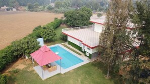 A two-story house with a swimming pool, a red-roofed gazebo, and a fenced yard. - Alaya Stays By Elivaas Luxe Farm Acre - Manesar (Taoru)