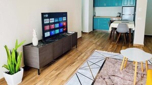 Una sala de estar moderna con televisor de pantalla plana, comedor con mesa y sillas, y cocina con armarios color turquesa.