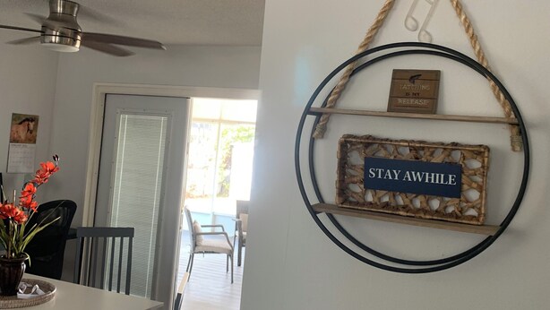 Un comedor con una mesa y sillas, un ventilador de techo y un adorno de pared con texto.
