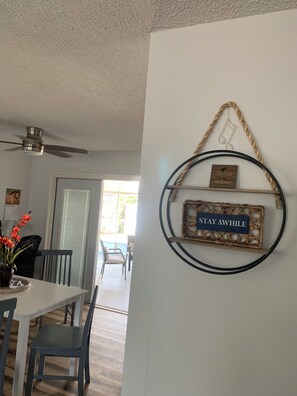 A dining area with a table and chairs, a ceiling fan, and a wall-mounted decorative item with text.