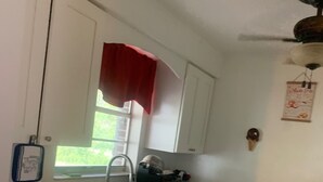 Una cocina pequeña con gabinetes blancos, un lavamanos de acero inoxidable y una ventana con cortina roja.