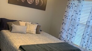 Un dormitorio con cama, ventilador de techo, ventana con cortinas y un cuadro en la pared con las fases de la luna.