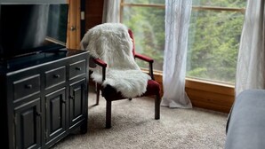 Una habitación acogedora con detalles de madera, un ventanal con cortinas, un televisor y un sillón mullido.