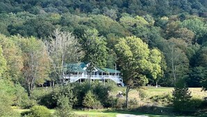 Una casa grande con techo verde, rodeada de árboles y un campo de golf.