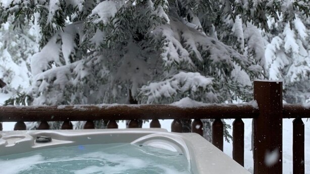 Un jacuzzi con un muelle de madera y árboles nevados al fondo.
