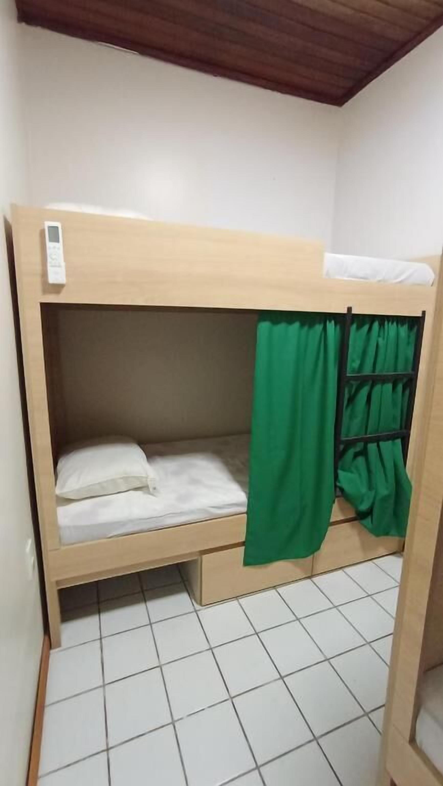 A bunk bed with a green curtain, white bedding, and a control panel on the headboard.