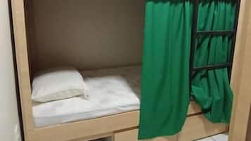 A bunk bed with a green curtain, white bedding, and a control panel on the headboard.