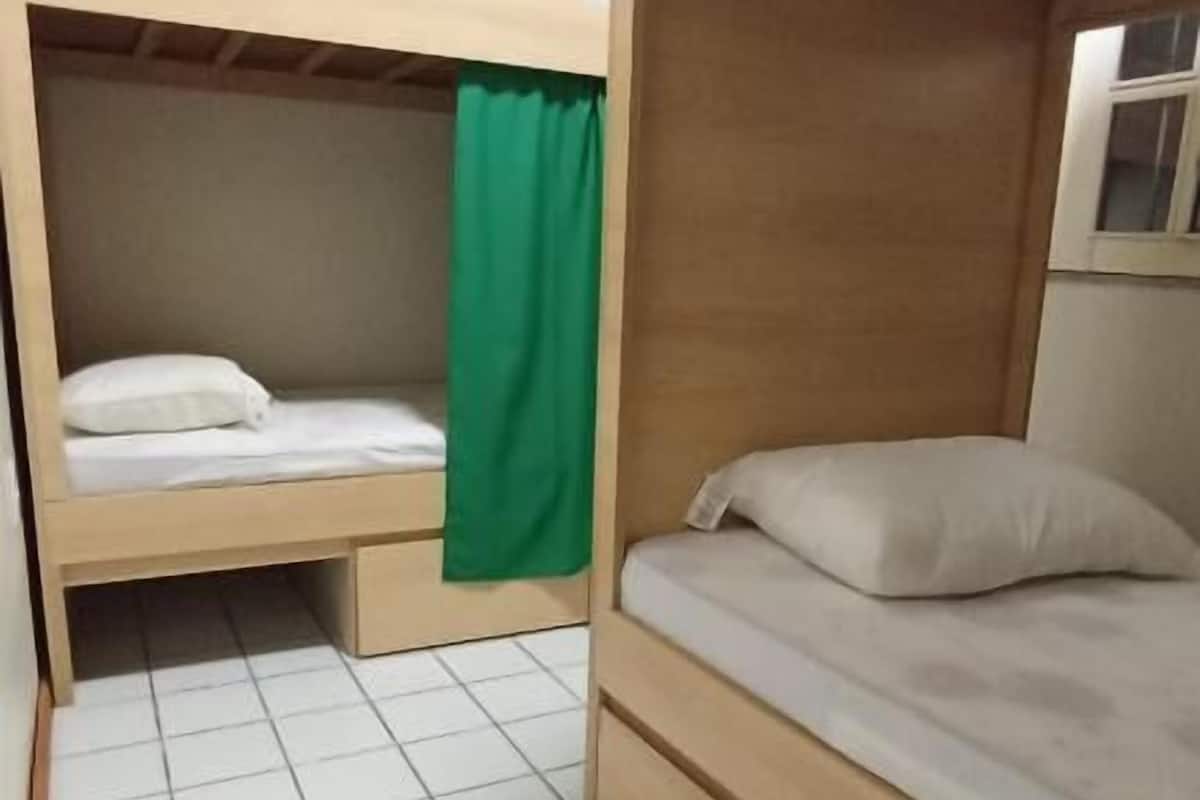 A compact room with two bunk beds, a green curtain, and a small window.