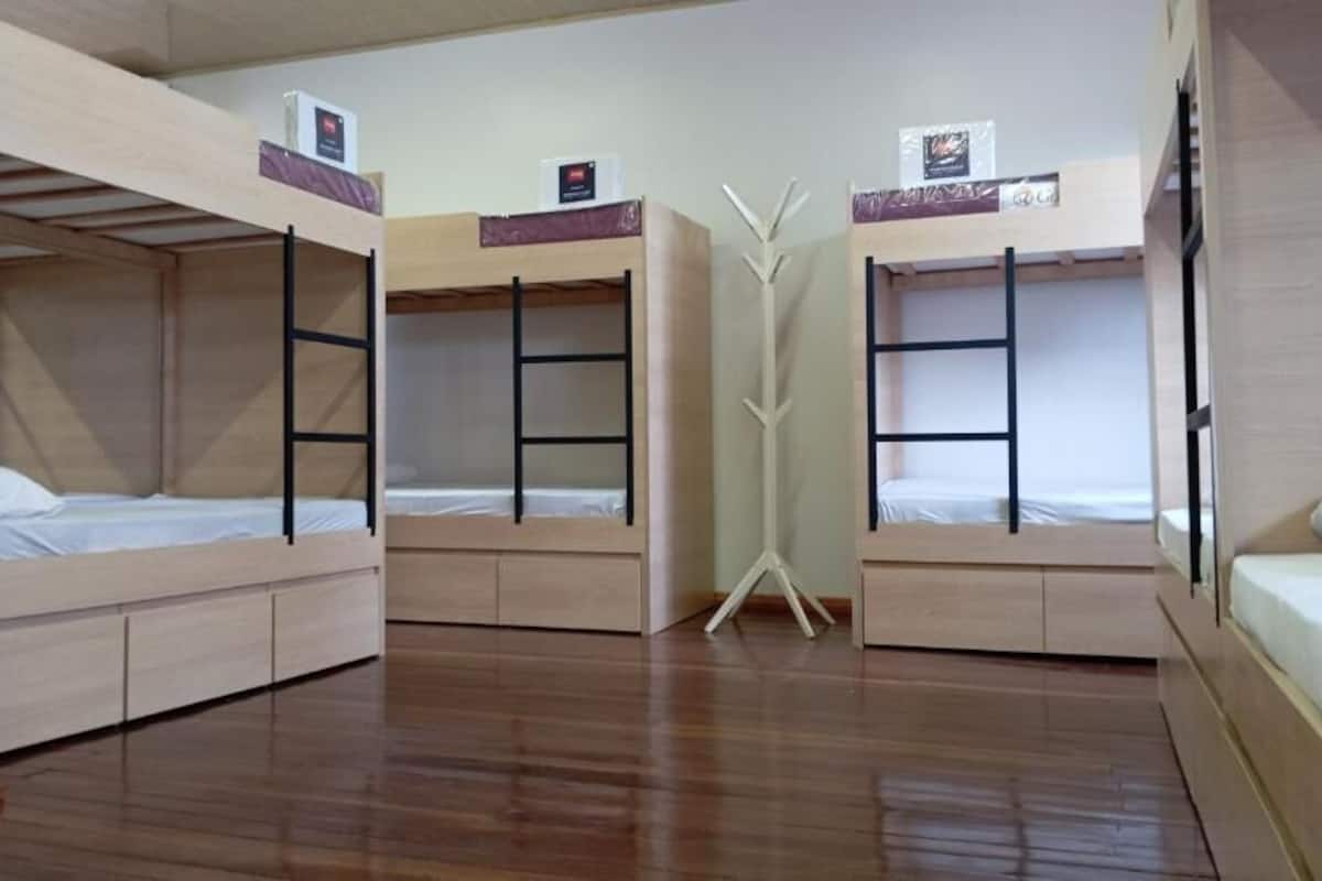 A room with bunk beds, a wooden floor, and a white coat rack.