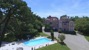 A large, historic mansion with a swimming pool, surrounded by lush greenery and a well-maintained lawn.