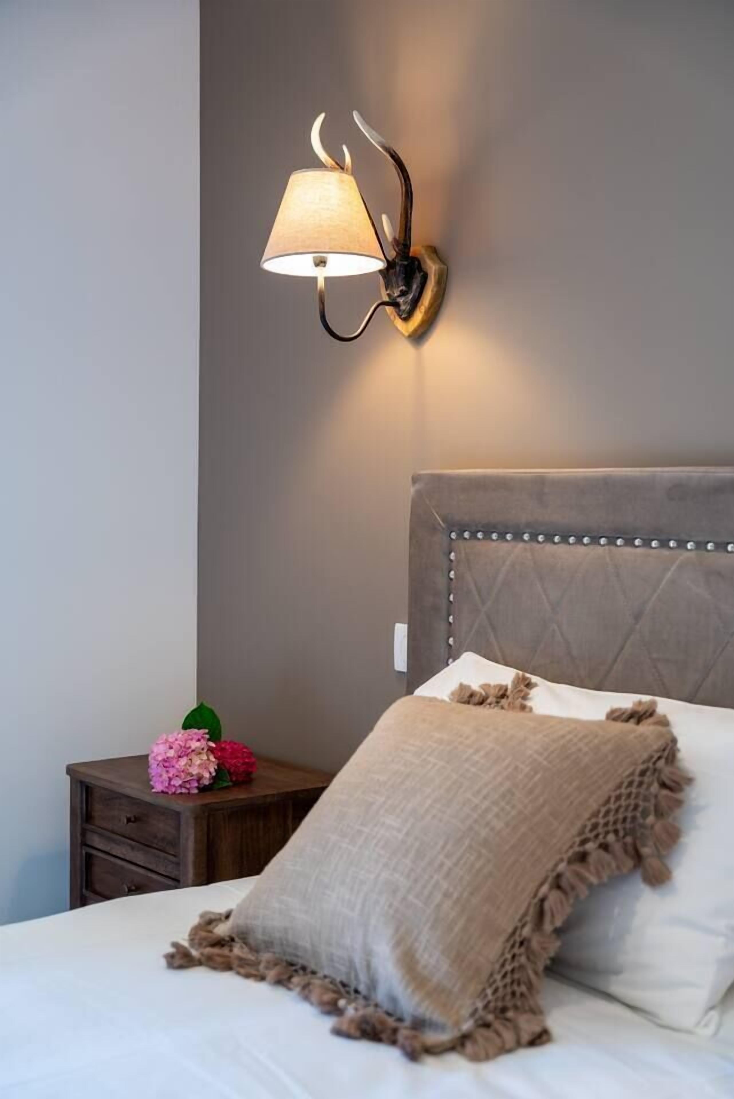 Quarto com uma cama, mesa de cabeceira, luminária na parede e um arranjo floral decorativo.