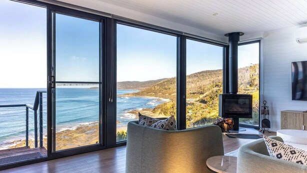 A modern living room with large glass doors leading to a coastal view, a fireplace, and a comfortable seating area. - The Nook - relaxing home breathtaking ocean views (Wye River)