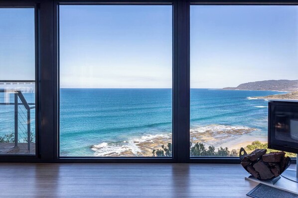 A room with large windows overlooking a coastal view, a wooden floor, and a small table with a decorative item.
