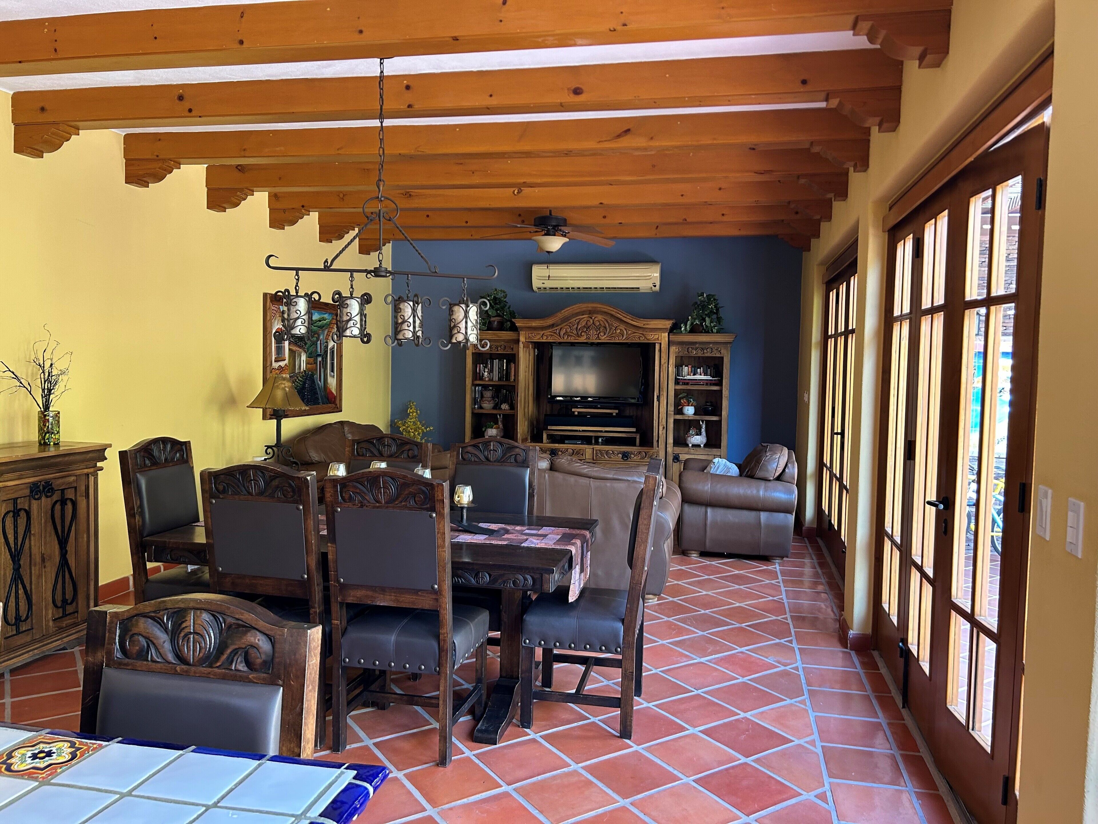 Ein geräumiges Wohnzimmer mit Holzbalkendecke, einem Essbereich mit Tisch und Stühlen, einer Couch und einem Fernseher.