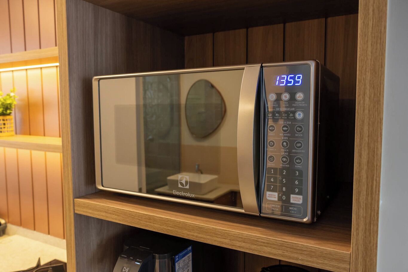 Forno de microondas com visor digital numa prateleira de madeira.