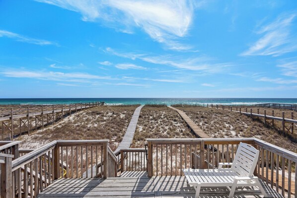 A wooden boardwalk leading to the beach with a white chair and a wooden railing.