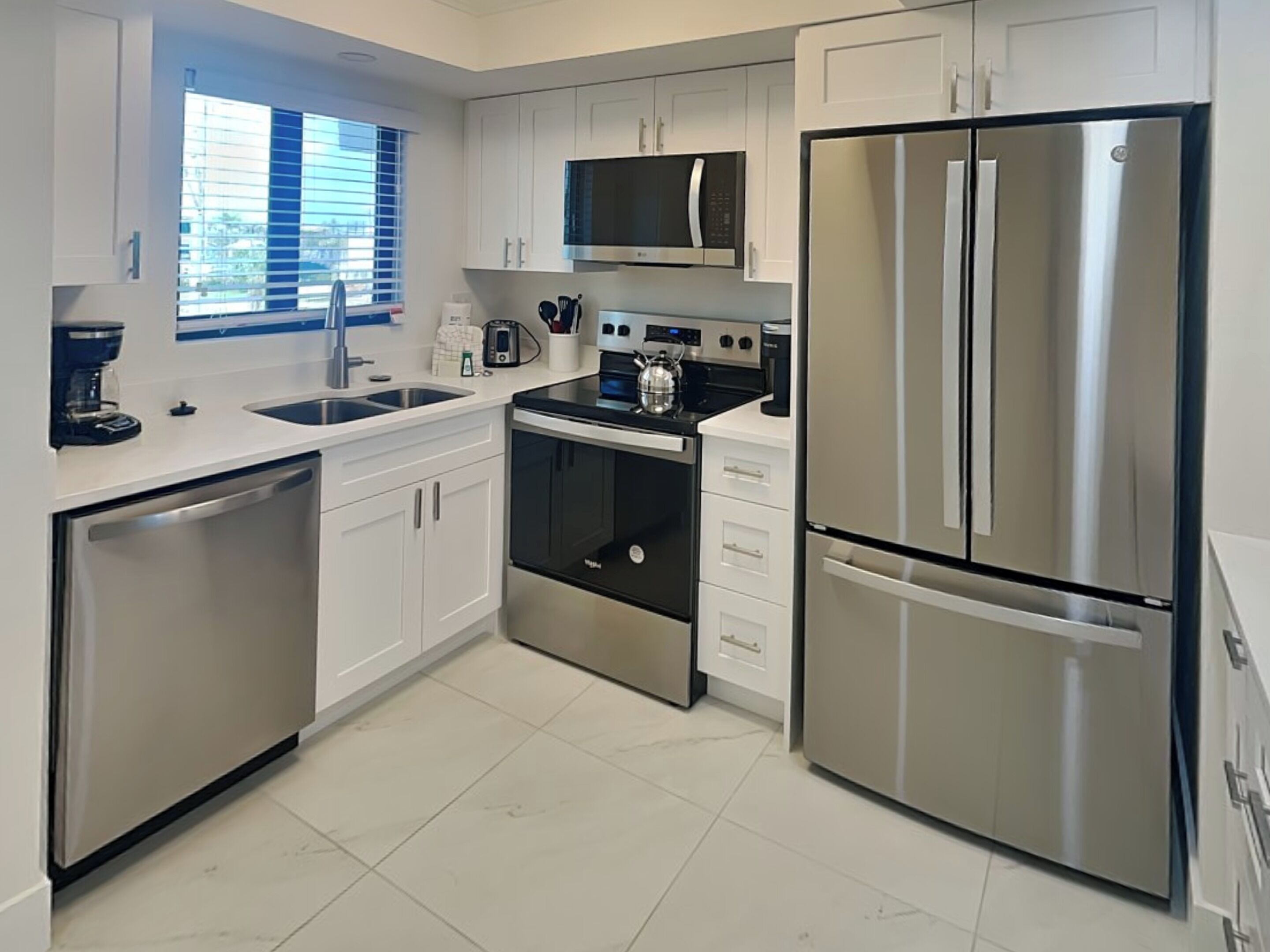 Una cocina moderna con gabinetes blancos, electrodomésticos de acero inoxidable, microondas, horno y refrigerador.