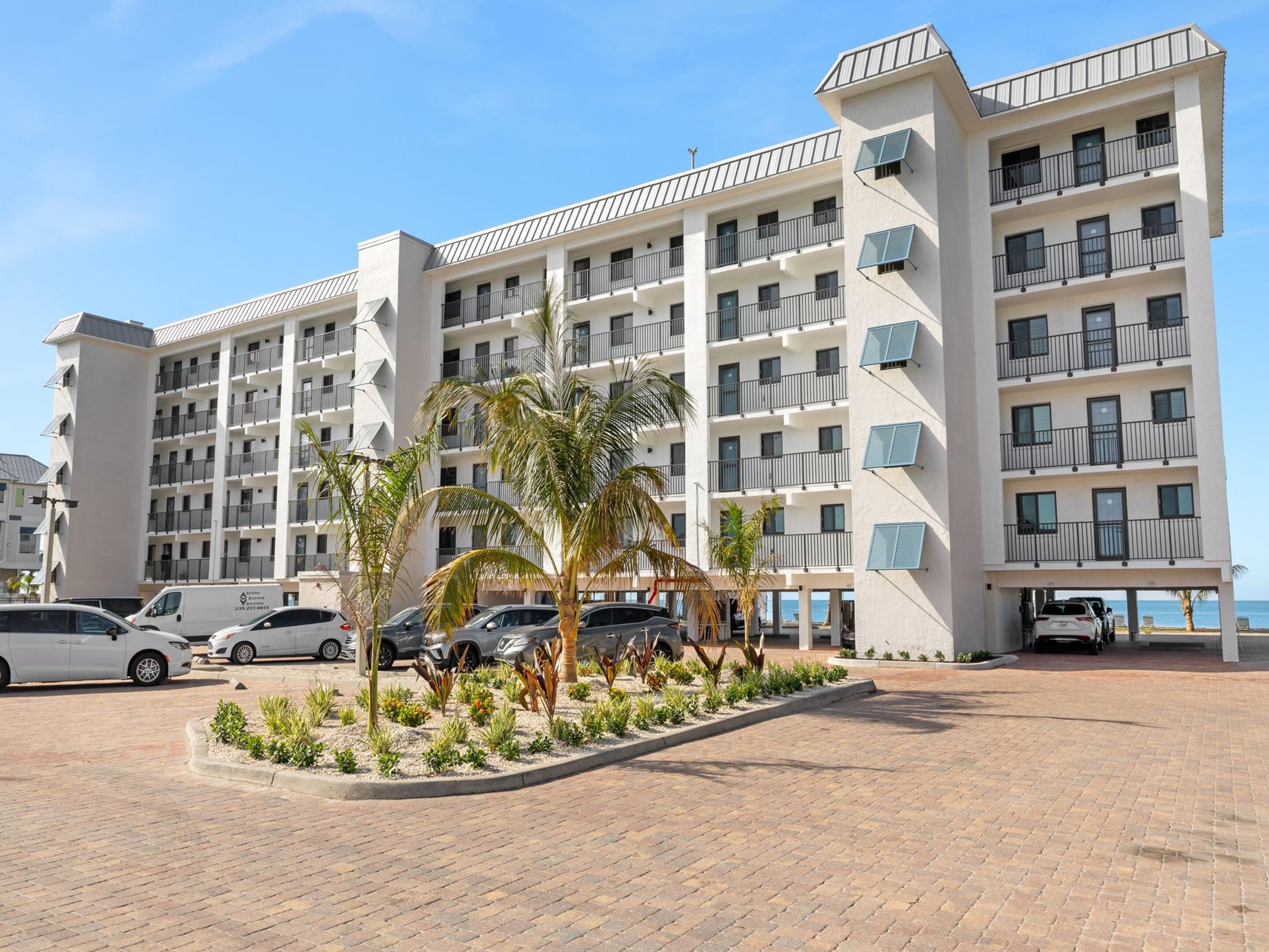 A multi-story hotel with balconies, a parking area, and palm trees.