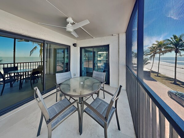 A balcony with a glass table and chairs, a ceiling fan, and a view of the beach. - Seaside 2 by Distinctive Beach Rentals (Fort Myers Beach)