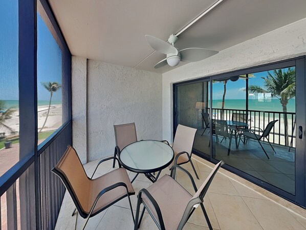A balcony with a glass door, a ceiling fan, and a view of the beach.