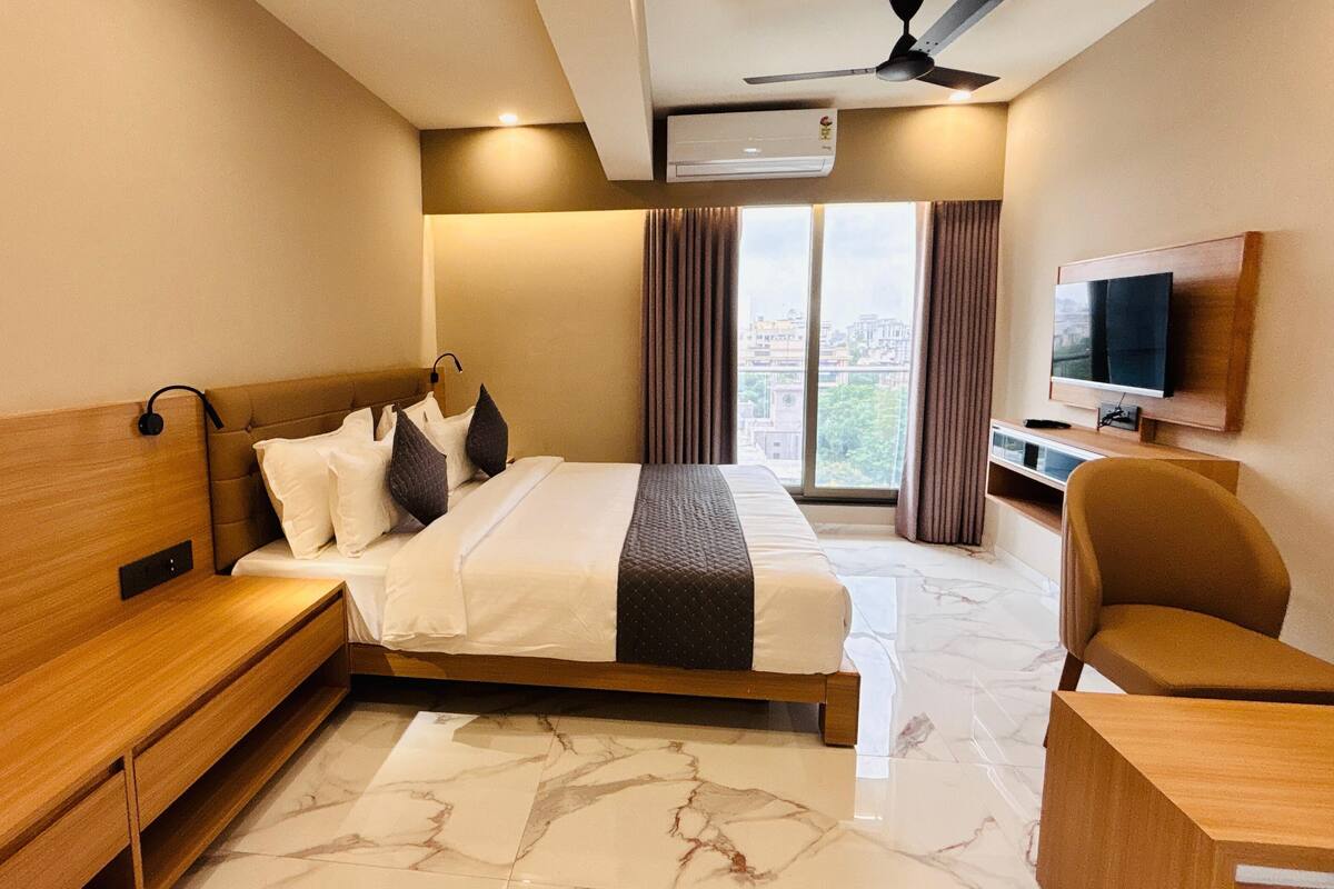 A hotel room with a bed, a desk, a chair, a TV, and a window with curtains.
