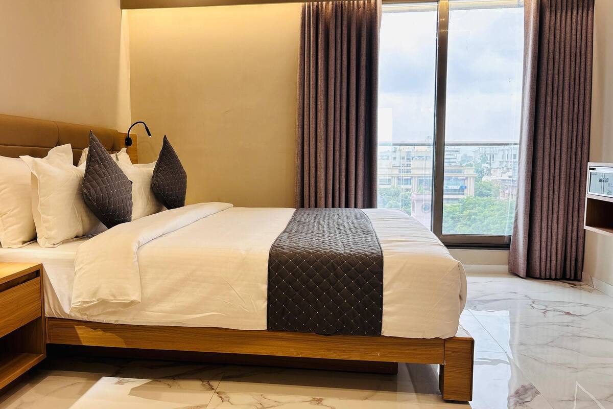 A modern bedroom with a wooden bed frame, a bedside table, and a large window with curtains.
