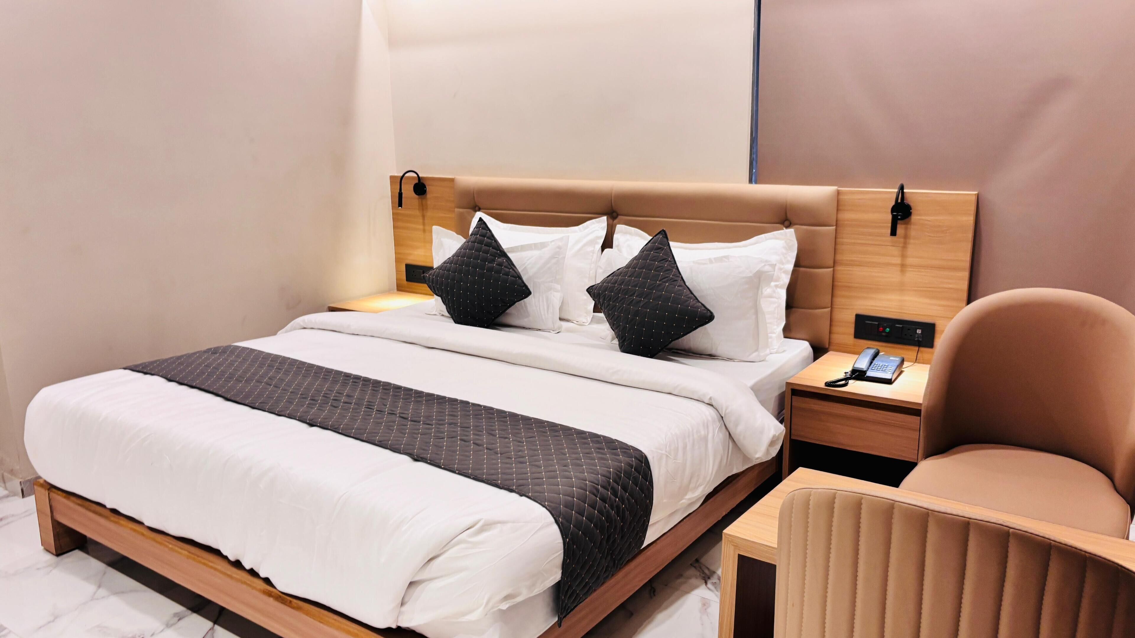 A modern hotel room with a large bed, two bedside tables, a chair, and a phone on one of the tables.