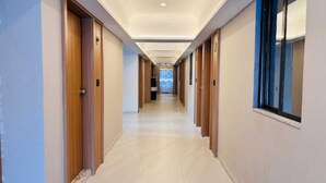 A long, narrow hallway with wooden doors on both sides, leading to a room with a large window.