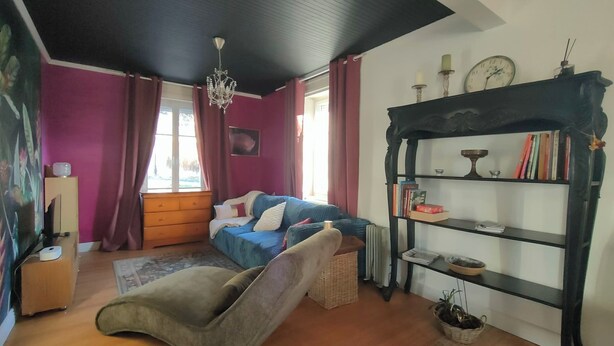 Een gezellige woonkamer met een blauwe bank, een houten vloer, een zwarte boekenkast en een kroonluchter.