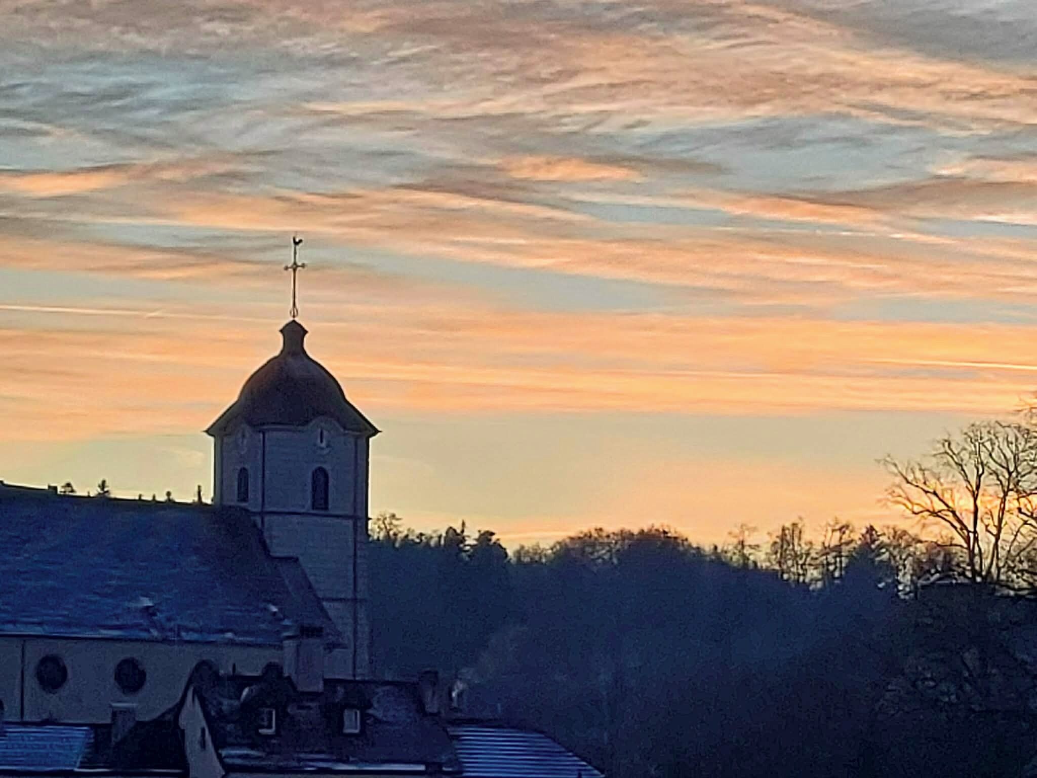 A church with a bell tower and a cross on top, surrounded by trees and buildings.