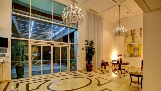 Un hall d’entrée doté d’une grande porte vitrée, d’un lustre, d’une plante en pot et d’une table avec des chaises.