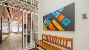 A hallway with a wooden bench, a geometric abstract painting, and a white gate leading to a covered area. - Apartamento Aconchegante a 850m da Av Paulista (São Paulo)