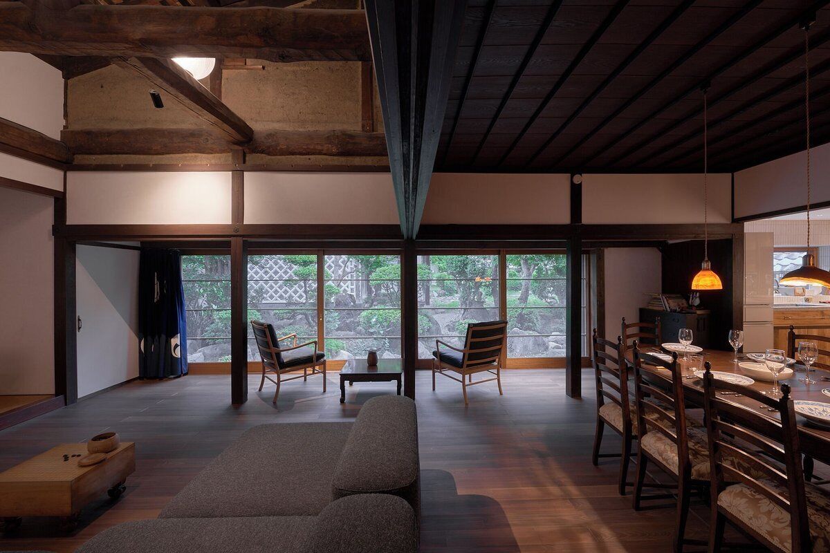 A spacious living area with a sofa, dining table, and chairs. There are large windows providing a view of the outdoors.