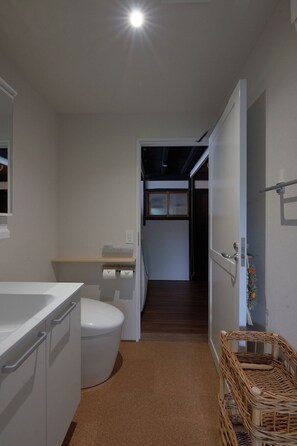 A narrow hallway leading to a staircase in a modern, minimalistic bathroom with a toilet, sink, and a small shelf. - Newly renovated entire villa, with serene gardens (Okaya-shi)