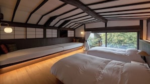 Una habitación con techos altos, vigas de madera a la vista, un banco largo con cojines y dos camas con sábanas blancas.