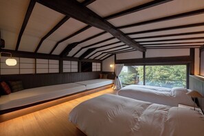 Una habitación con techos altos, vigas de madera a la vista, un banco largo con cojines y dos camas con sábanas blancas.