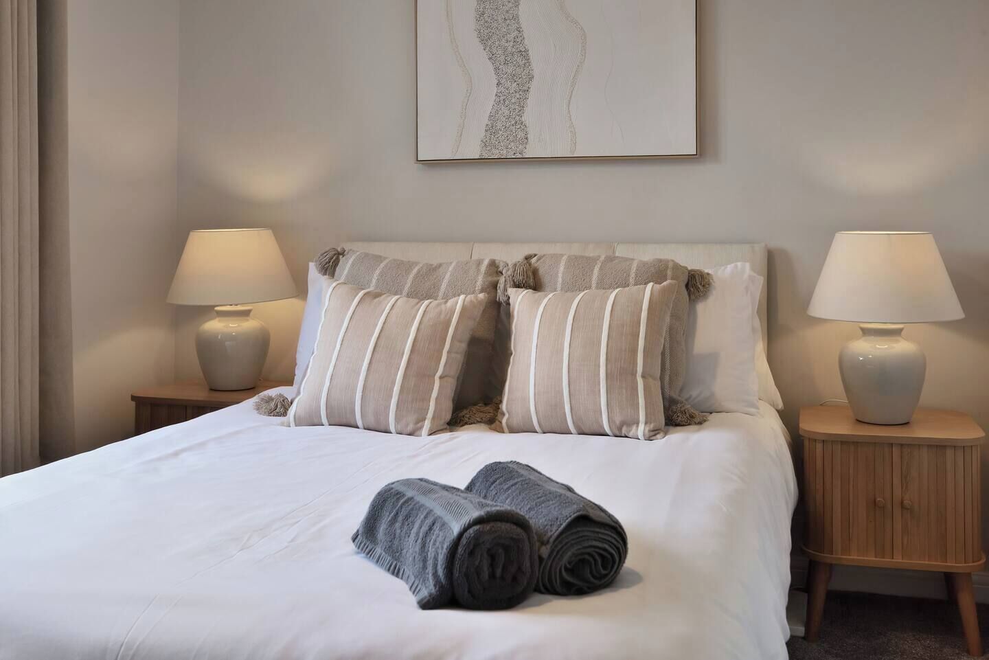 A neatly made bed with striped pillows, two bedside lamps, and a rolled towel on the bed.