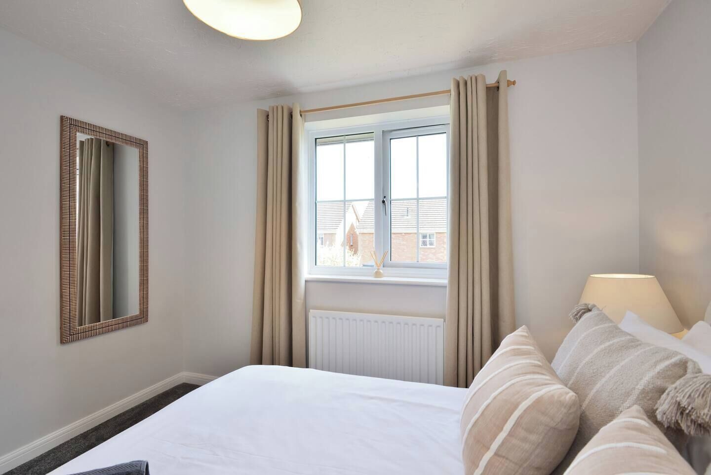 A hotel room with a large bed, a window with curtains, a radiator, and a lamp on the bedside table.