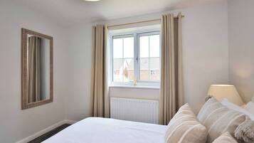 A hotel room with a large bed, a window with curtains, a radiator, and a lamp on the bedside table.